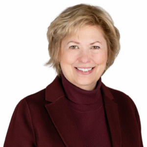 A person with short blond hair wearing a maroon turtleneck and jacket smiles against a white background.